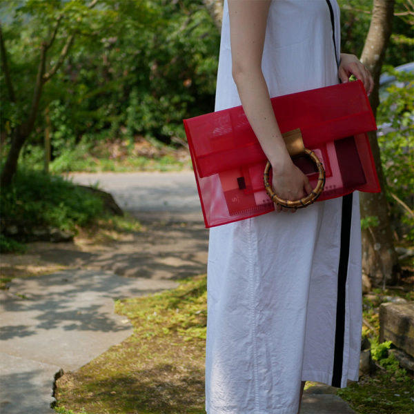 赤色の竹クラッチバッグを持つ女性